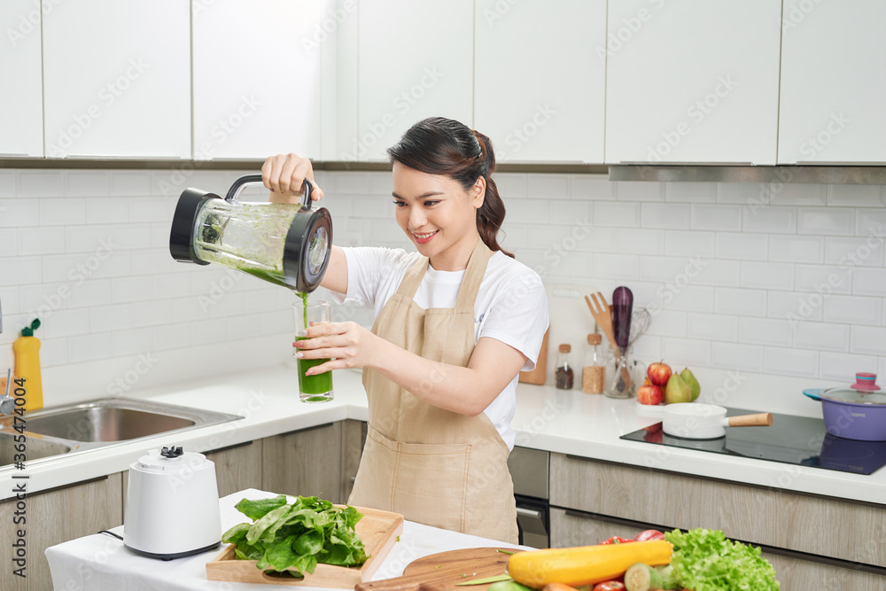 快乐女人排毒减肥，把绿色鸡尾酒从搅拌机里倒进厨房的玻璃里