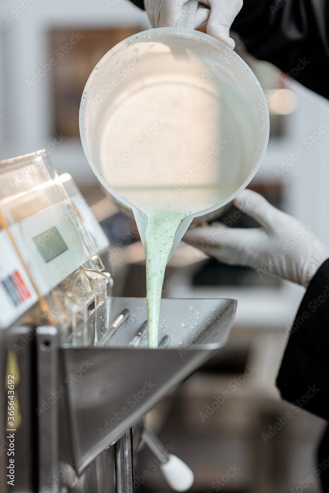 Chef pouring mixed milk base into the ice cream machine or freezer, close-up