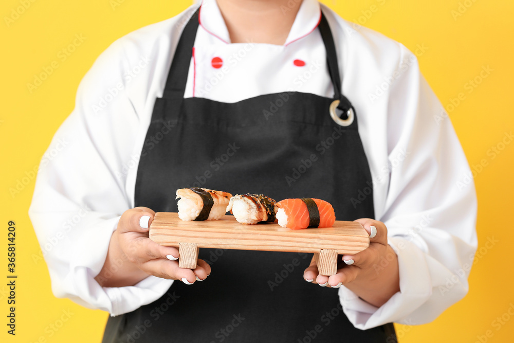 Beautiful Asian chef with sushi rolls on color background