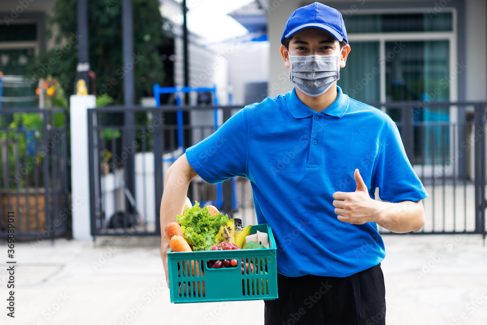 亚洲送货员身穿蓝色制服，戴医用口罩，为杂货店提供新鲜食品t