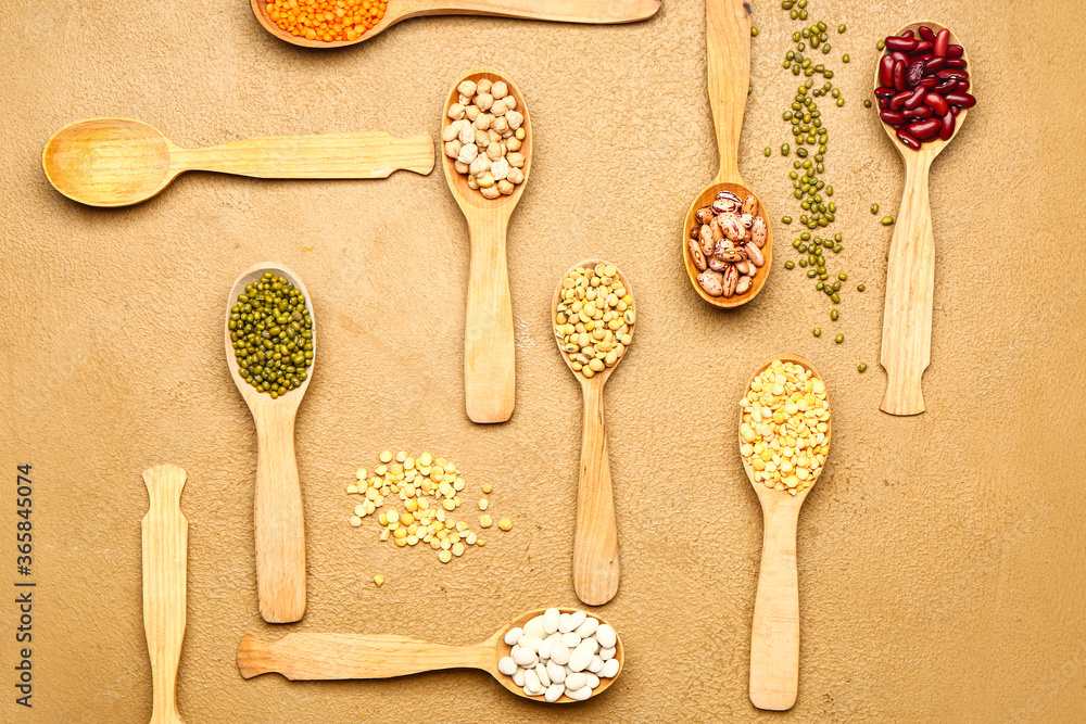 Spoons with raw legumes on color background