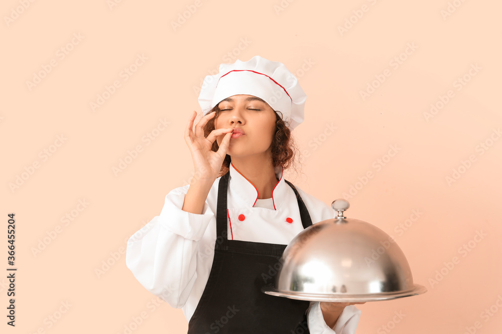 Female African-American chef with tray and cloche on color background