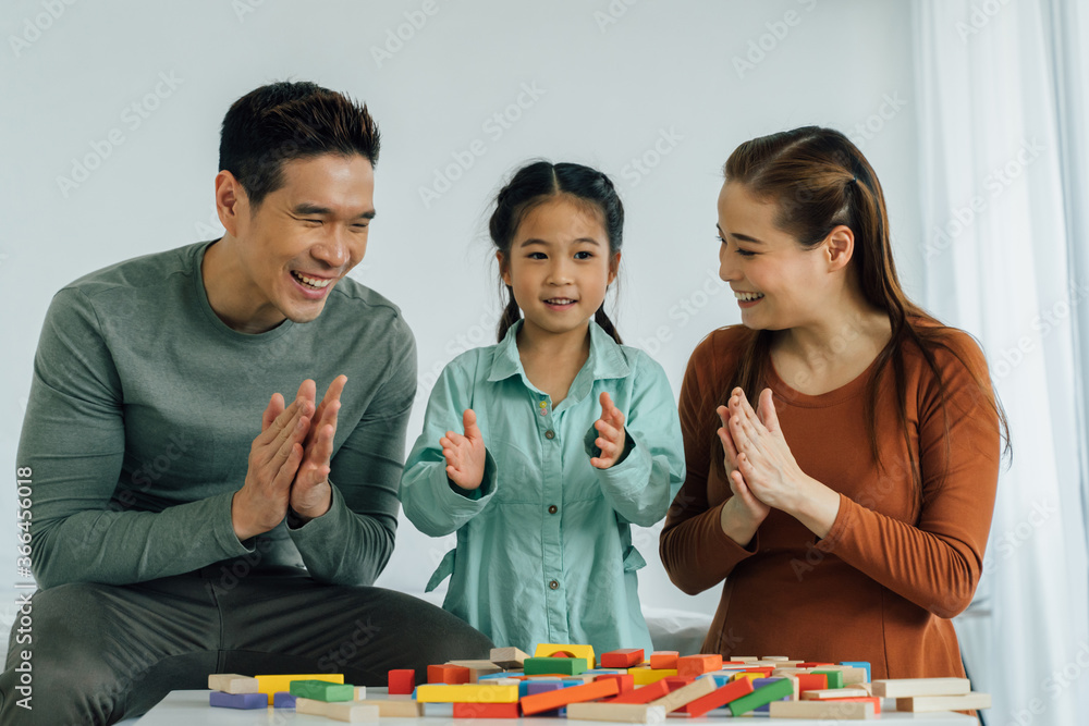 快乐的中国父母带着年幼的女儿玩木制积木和拍手