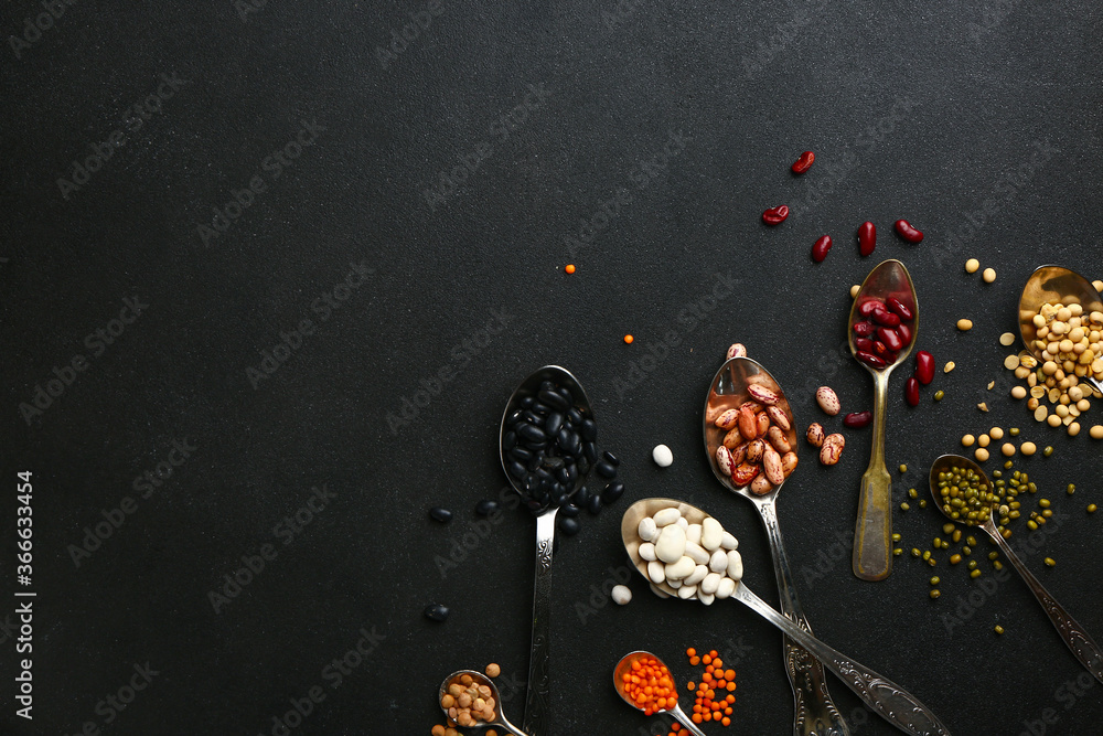 Spoons with raw beans on dark background