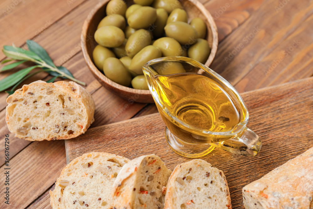 Gravy boat of tasty olive oil and bread on wooden background