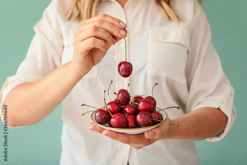 Woman with plate of sweet cherry on color background, closeup