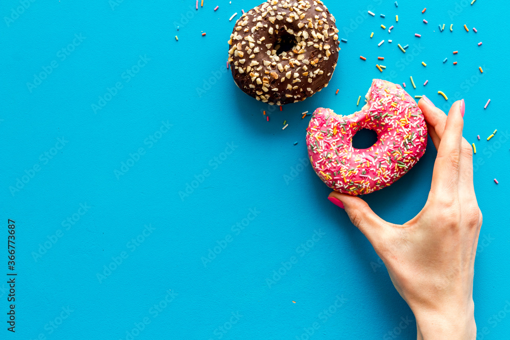 Hand holding donut with icing and sprinkles. Flat lay, top view