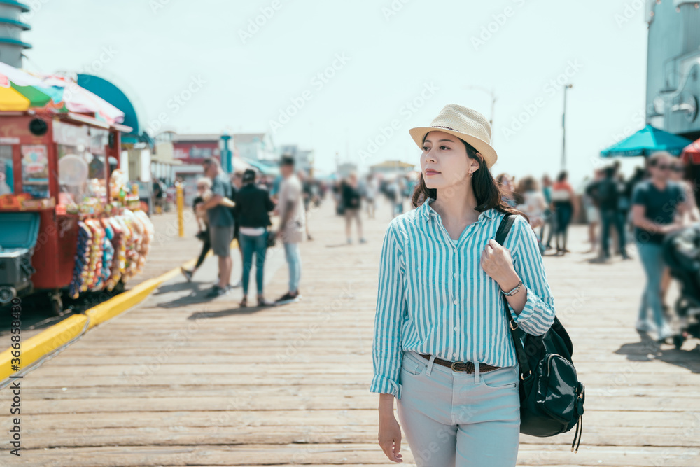 年轻漂亮的女士游客戴着草帽，背着背包在圣莫尼游乐园散步