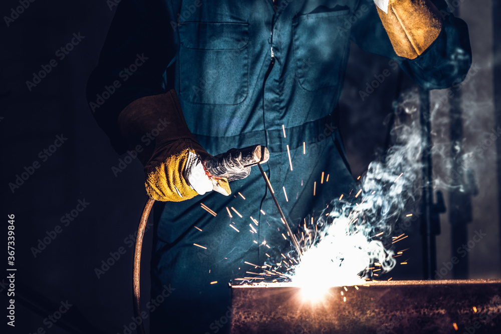 Metal welder working with arc welding machine to weld steel at factory while wearing safety equipmen