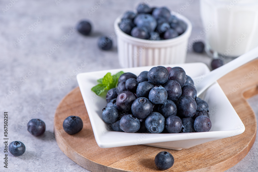 Pile of blueberry fruit in a bowl plate on a tray over gray cement concrete background, close up, he