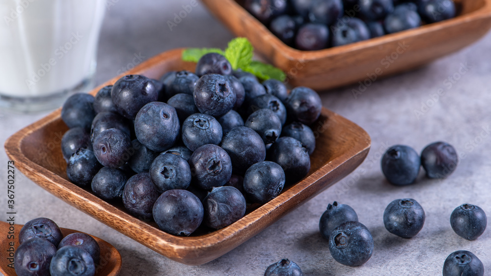 Pile of blueberry fruit in a bowl plate on a tray over gray cement concrete background, close up, he