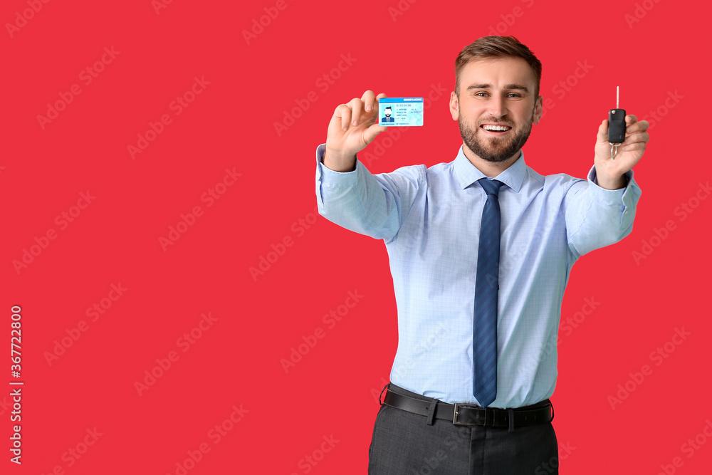 Happy young businessman with car key and driving license on color background