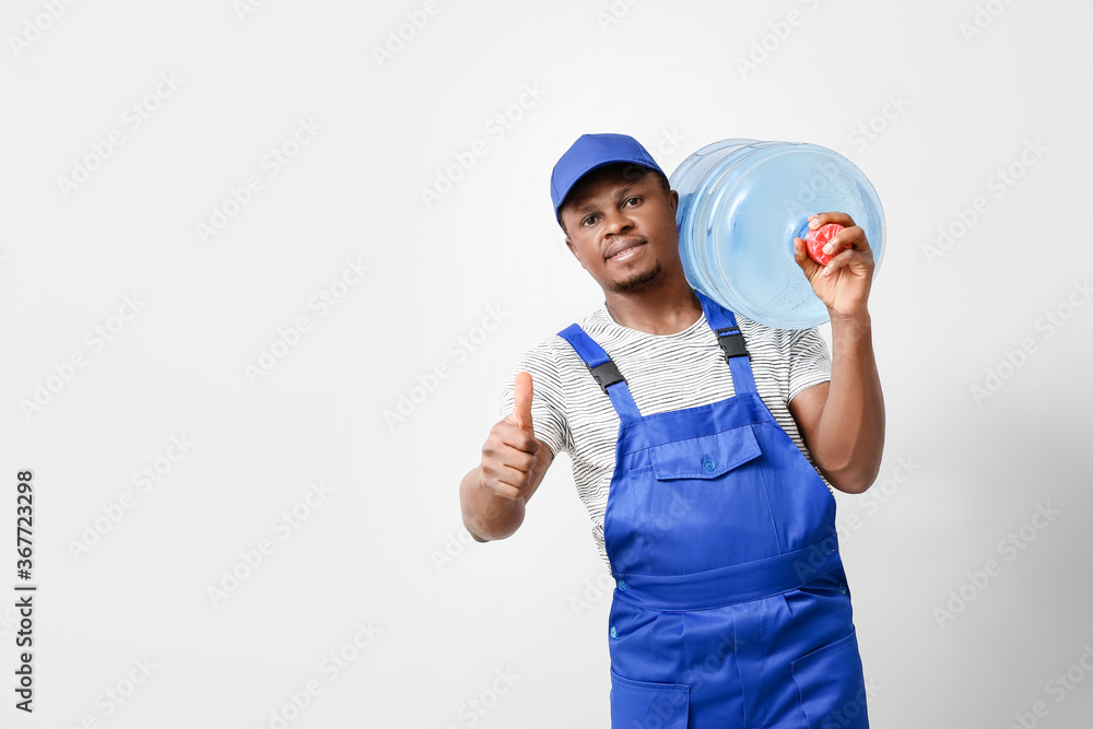 African-American delivery man with bottle of water showing thumb-up gesture on light background