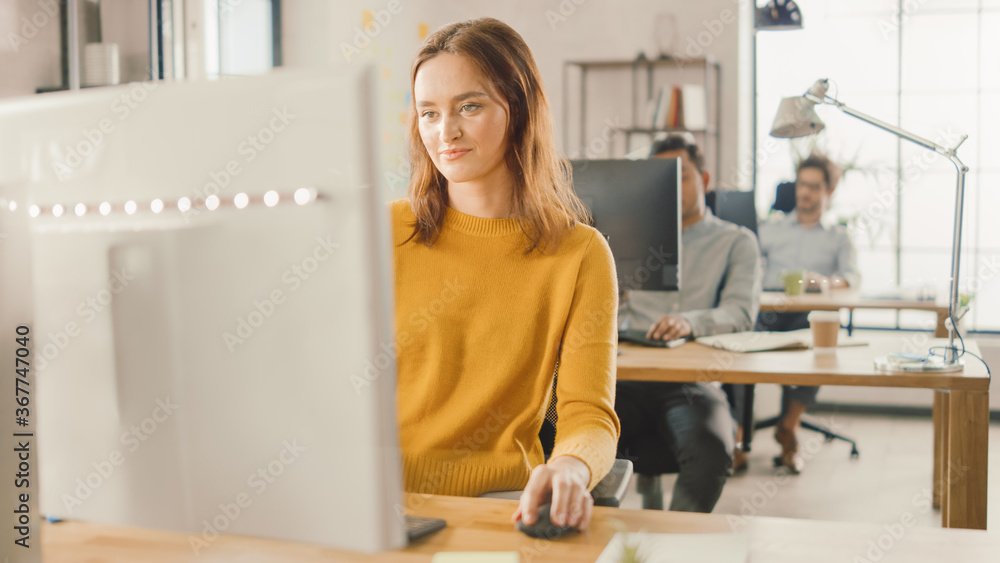 Beautiful and Smart Red Haired Female Specialist Sitting at Her Desk Works on a Desktop Computer. In