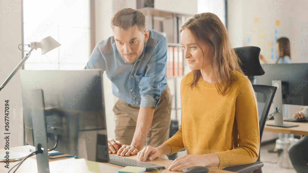 Female Specialist Works on Desktop Computer, Project Manager Stands Beside and gives Advice on Optim