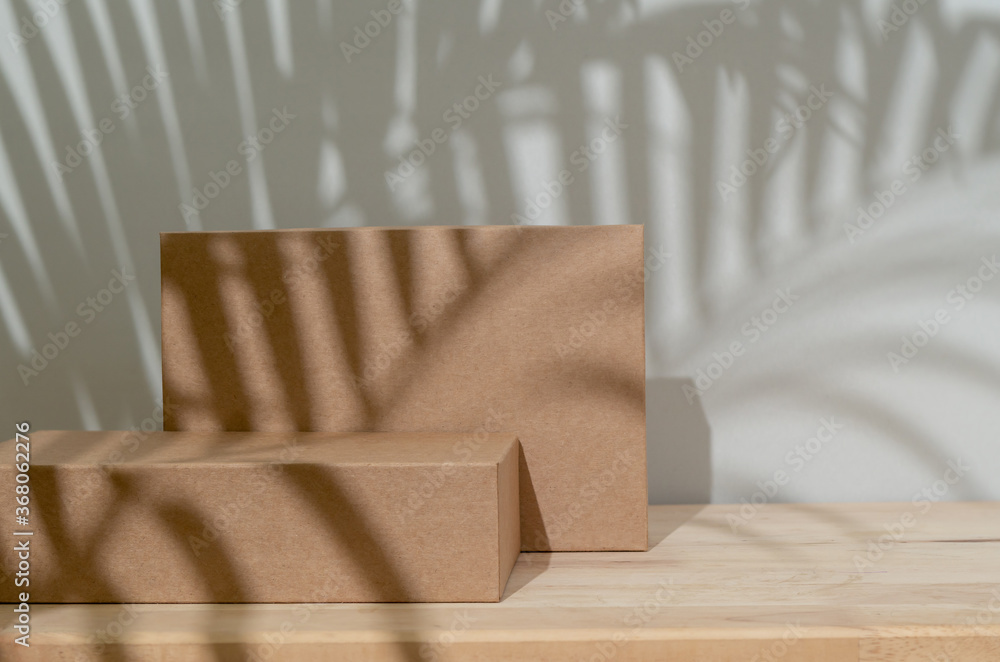 Brown podium stage from paper box on wooden table on white background with shadows of palm leaf for 