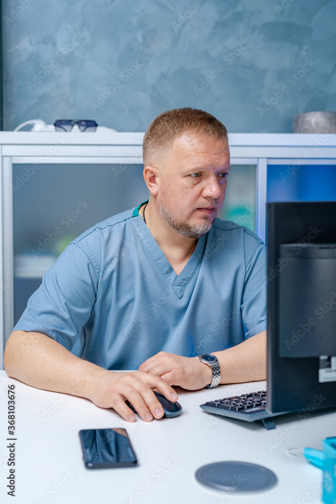 Doctor in blue scrubs sitting near computer. Searching medical information. Diagnostic and medical c