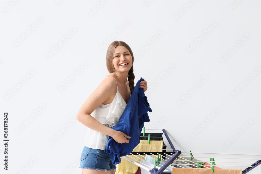 Woman hanging clean clothes on dryer against light background