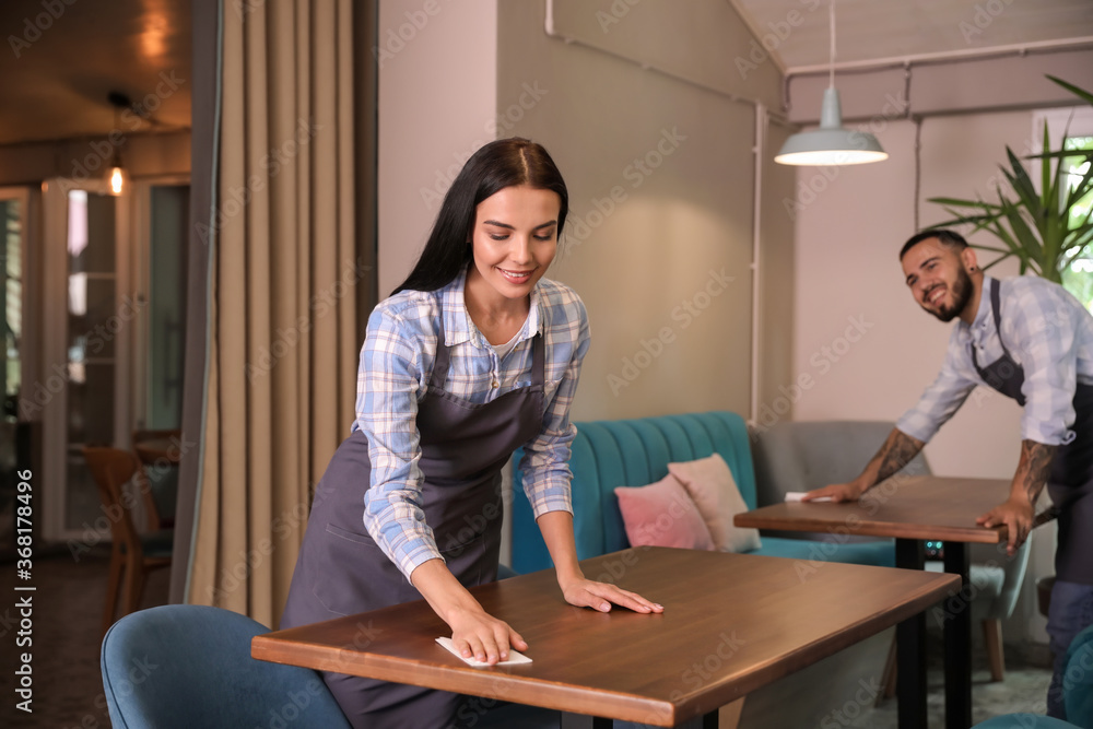 Young waitress cleaning table in restaurant