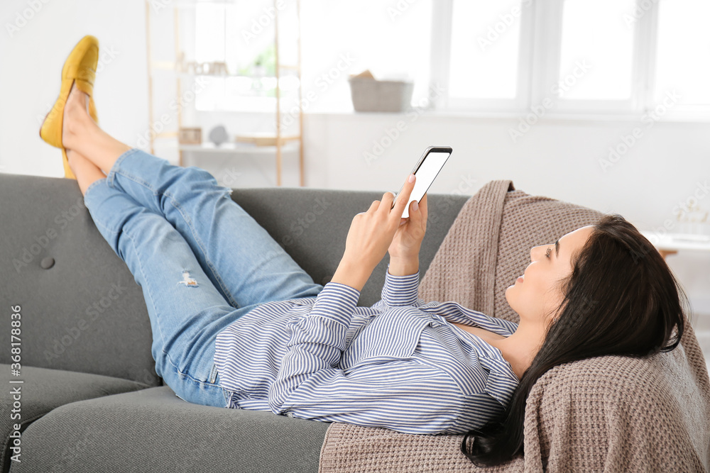 Young woman with mobile phone relaxing on sofa at home