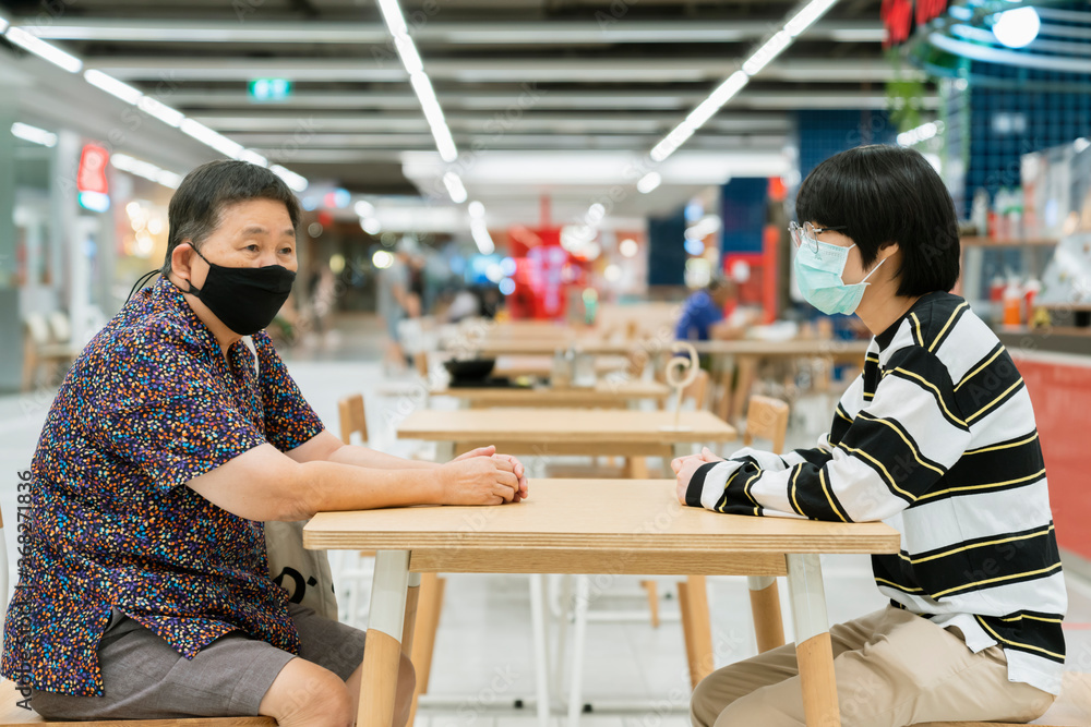 老年女性和年轻侄子坐着聊天，保持距离——封锁后的新常态生活方式