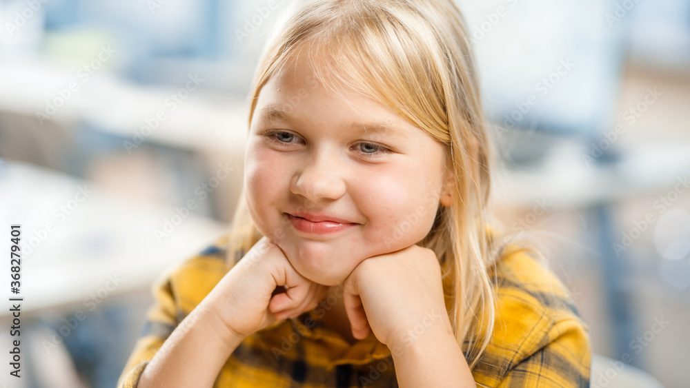 Portrait of a Cute Little Girl with Blond Hair Sitting at her School Desk, Smiles Happily. Smart Lit