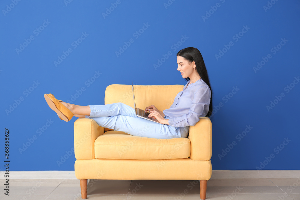 Young woman with laptop relaxing in armchair at home