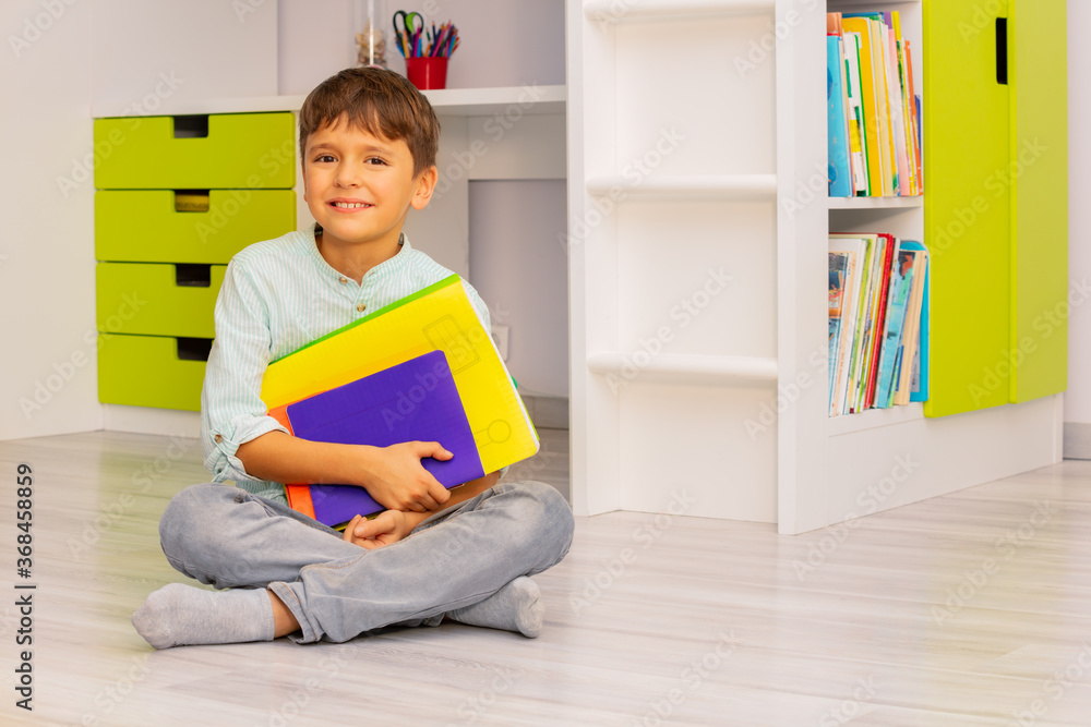 Smiling calm little boy sit in his room holding textbooks with positive expression