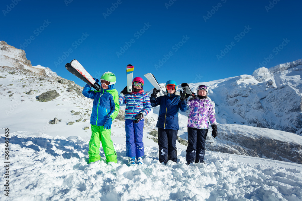 肩上扛着滑雪运动装备的男孩和一群朋友一起站在背后的山峰上