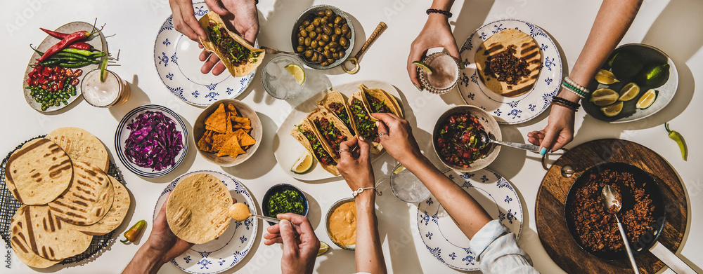 Friends having Mexican Taco dinner. Flat-lay of beef tacos, tomato salsa, tortillas, beer, nachos an