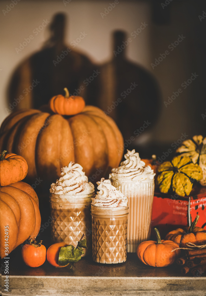 Pumpkin spicy latte coffee drink topped with whipped cream in glasses among fresh pumpkins, persimmo