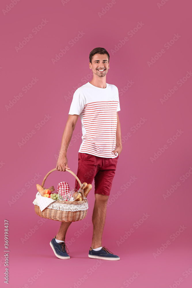 Young man with food for picnic in basket on color background