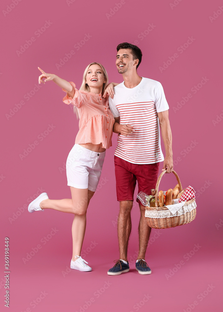 Young couple with food for picnic in basket on color background