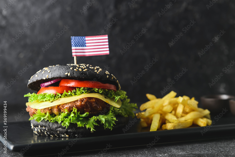 Tasty burger with black bun and french fries on dark background