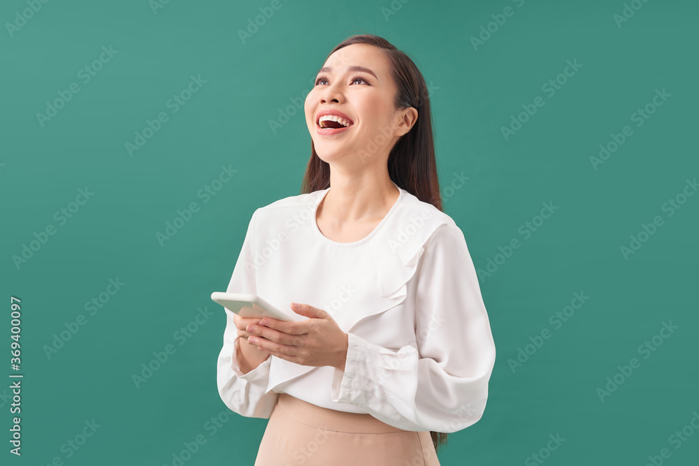 Portrait of a laughing asian businesswoman using mobile phone isolated over turquoise  background