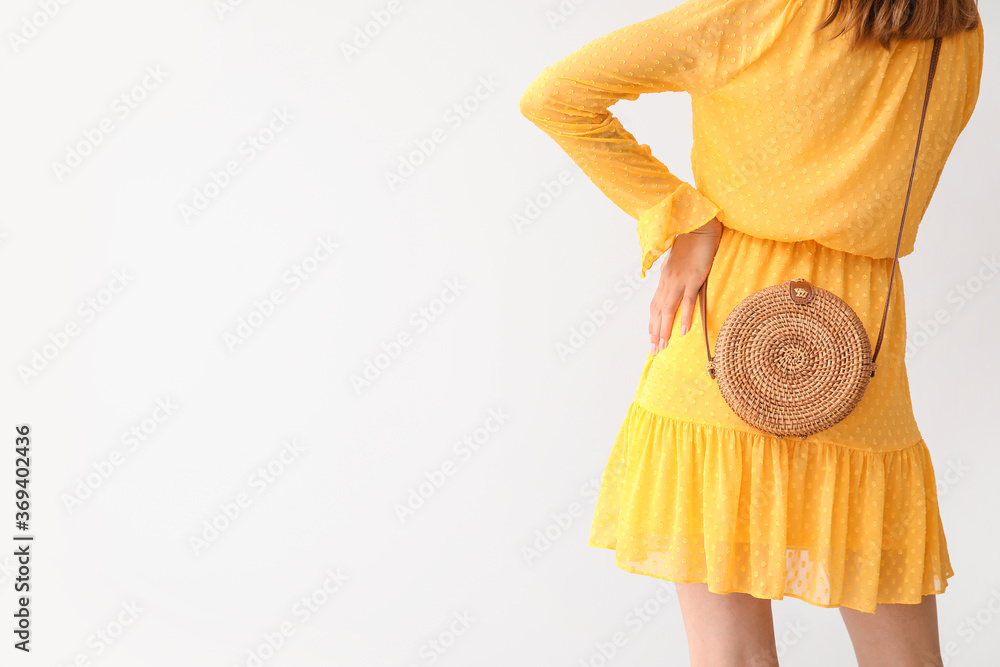 Beautiful young woman with wicker bag on light background