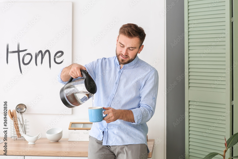 Man pouring hot boiled water from electric kettle into cup at home