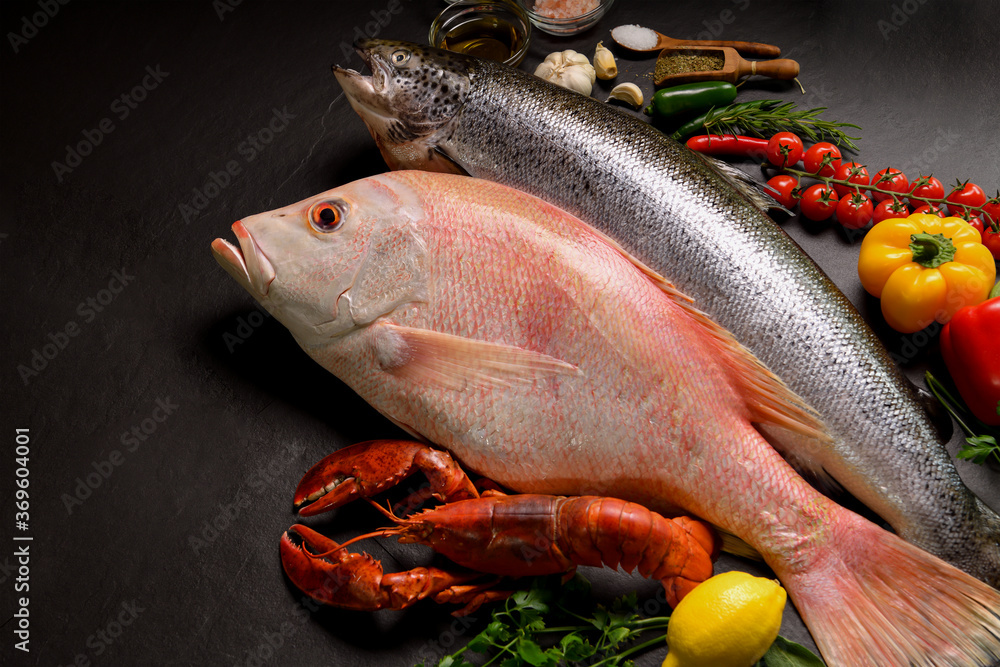 Top view of variety of fresh fish and seafood on black stone background