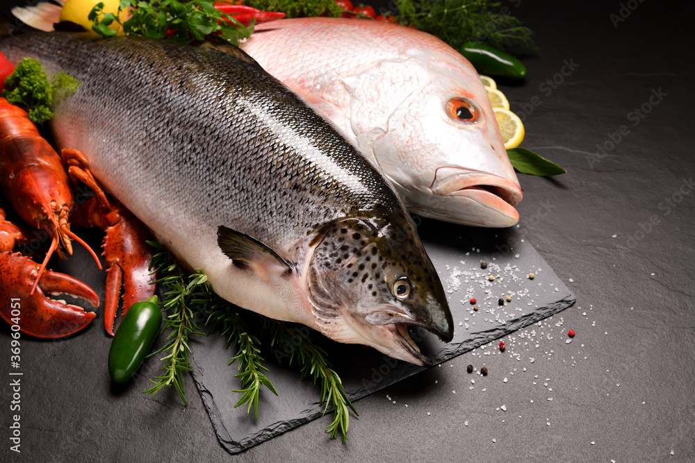 Fresh raw fish and seafood arranged on black stone background