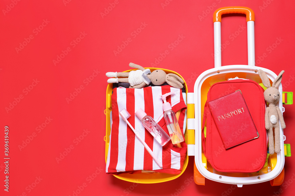 Suitcase with travel accessories for children on color background