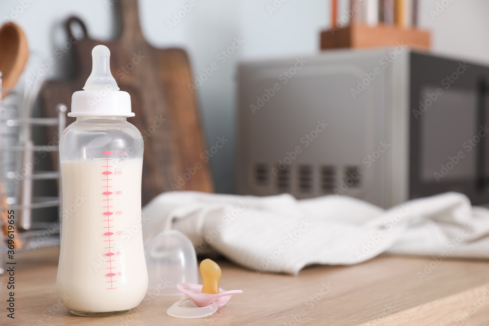 Bottle of milk for baby, pacifier and clothes on table