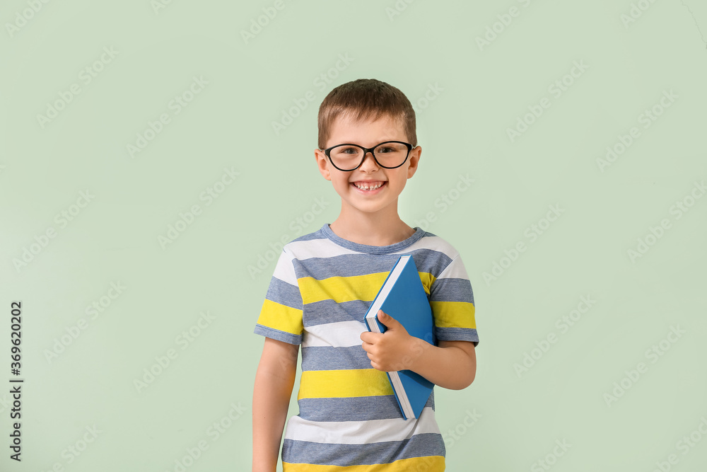 Cute little boy with book on color background