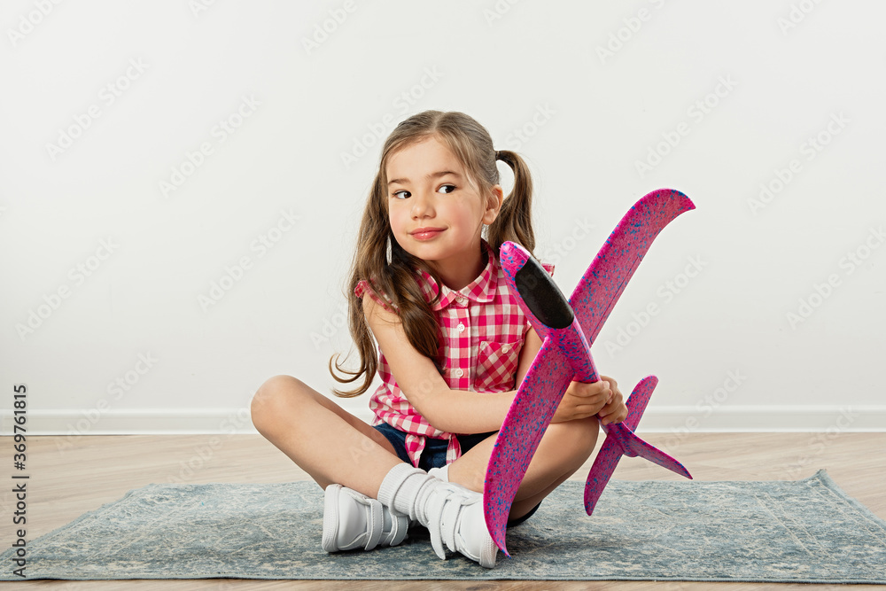 girl sits on  carpet and holds pink plane in her hands, travel concept