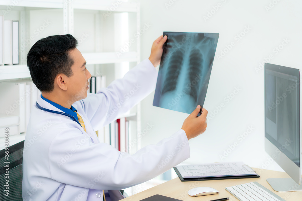 Asian man doctor holding and looking to examining x-ray of the patient’s lungs and brain in a medica