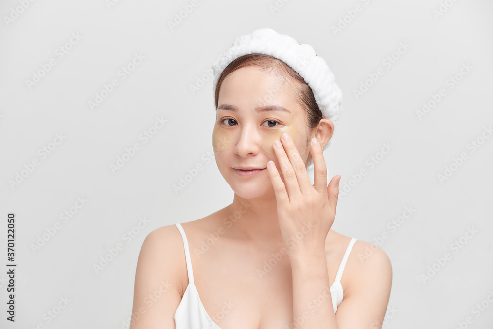 Portrait of young Asian woman applying cream on her face over white background