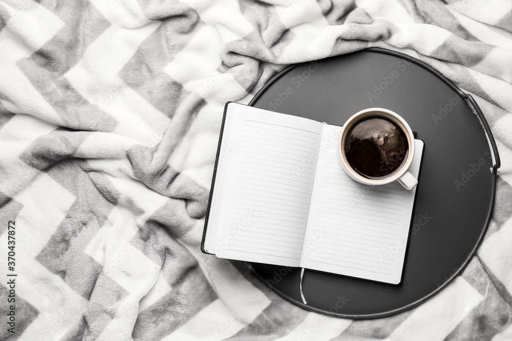 Tray with cup of coffee and book on plaid