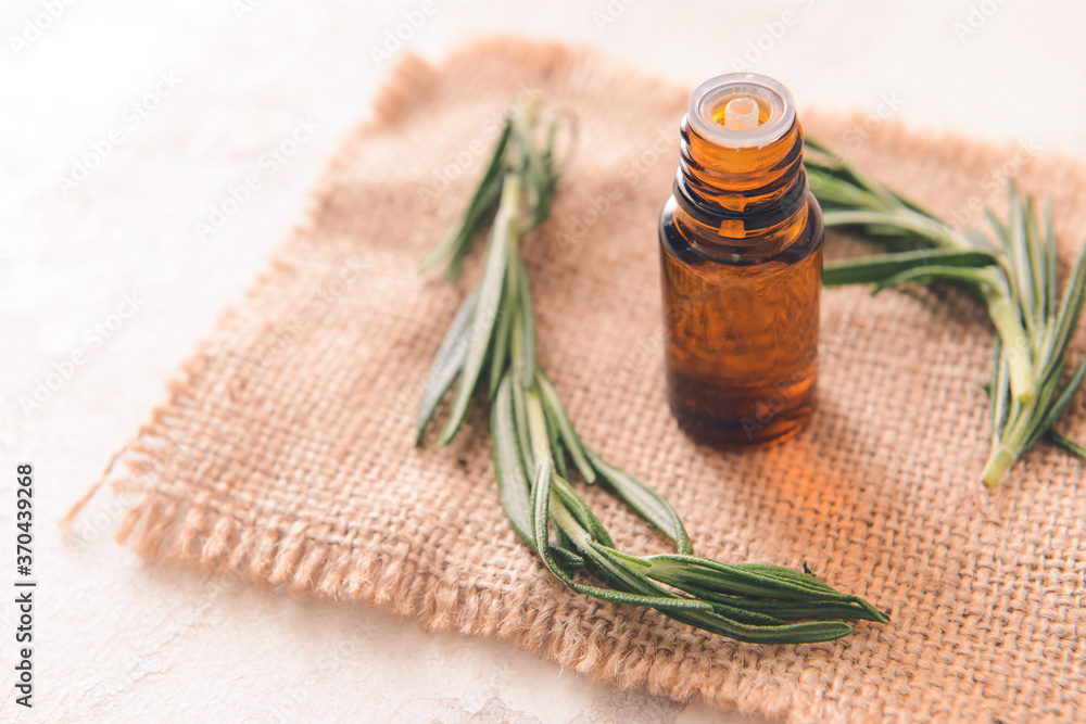 Bottle of rosemary essential oil on light background