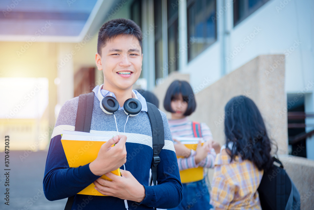 年轻的亚洲男青少年学生站在学校微笑。