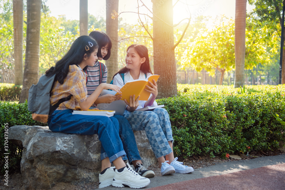 三个亚洲少女坐在公园里，一起用笔记本电脑做作业。