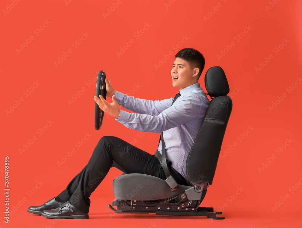 Displeased Asian businessman with steering wheel sitting on car seat against color background